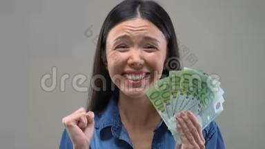 兴奋的亚洲女士向镜头展示了一堆欧元，彩票<strong>中奖</strong>者，财富